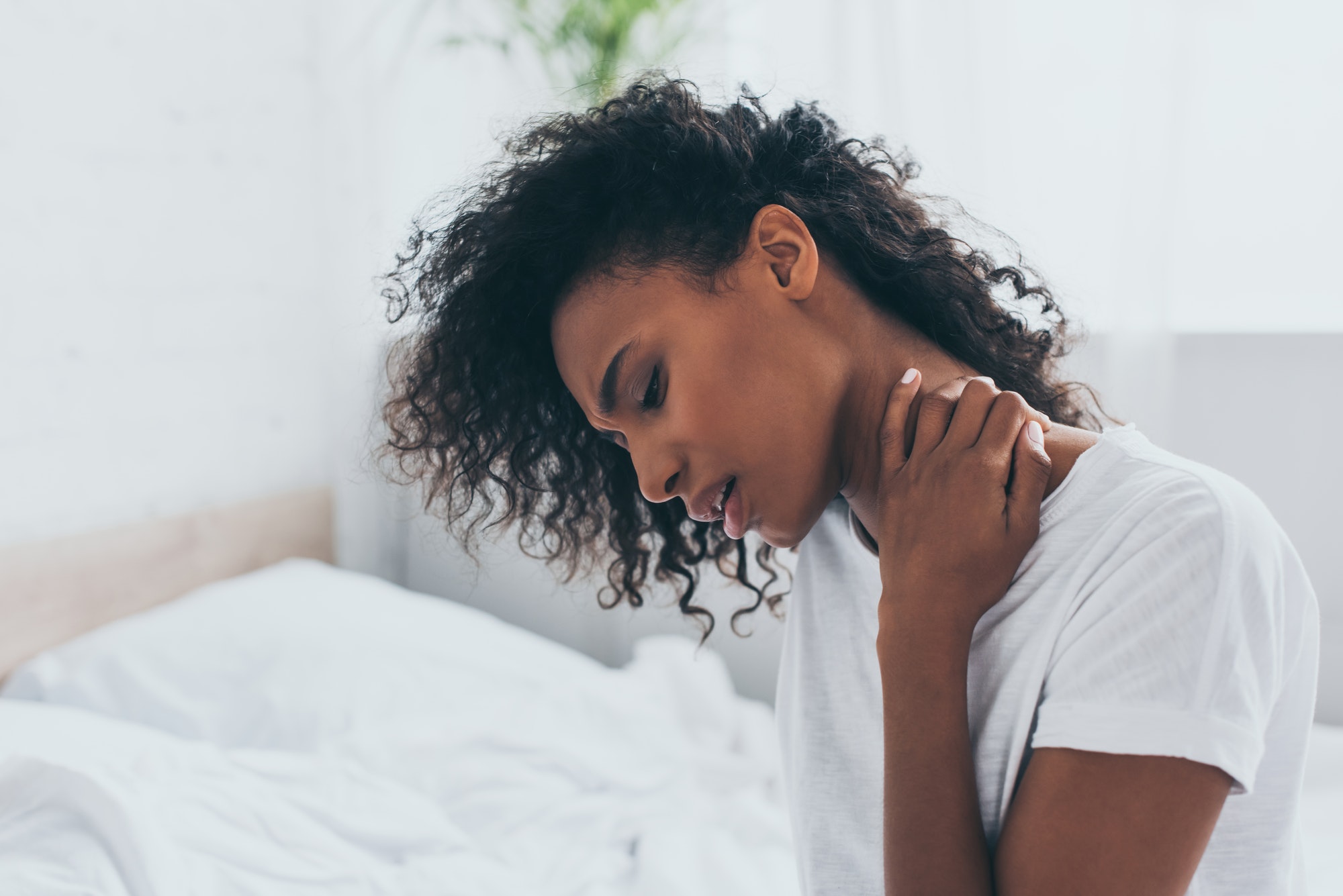 unhappy african american woman suffering from neck pain in bedroom